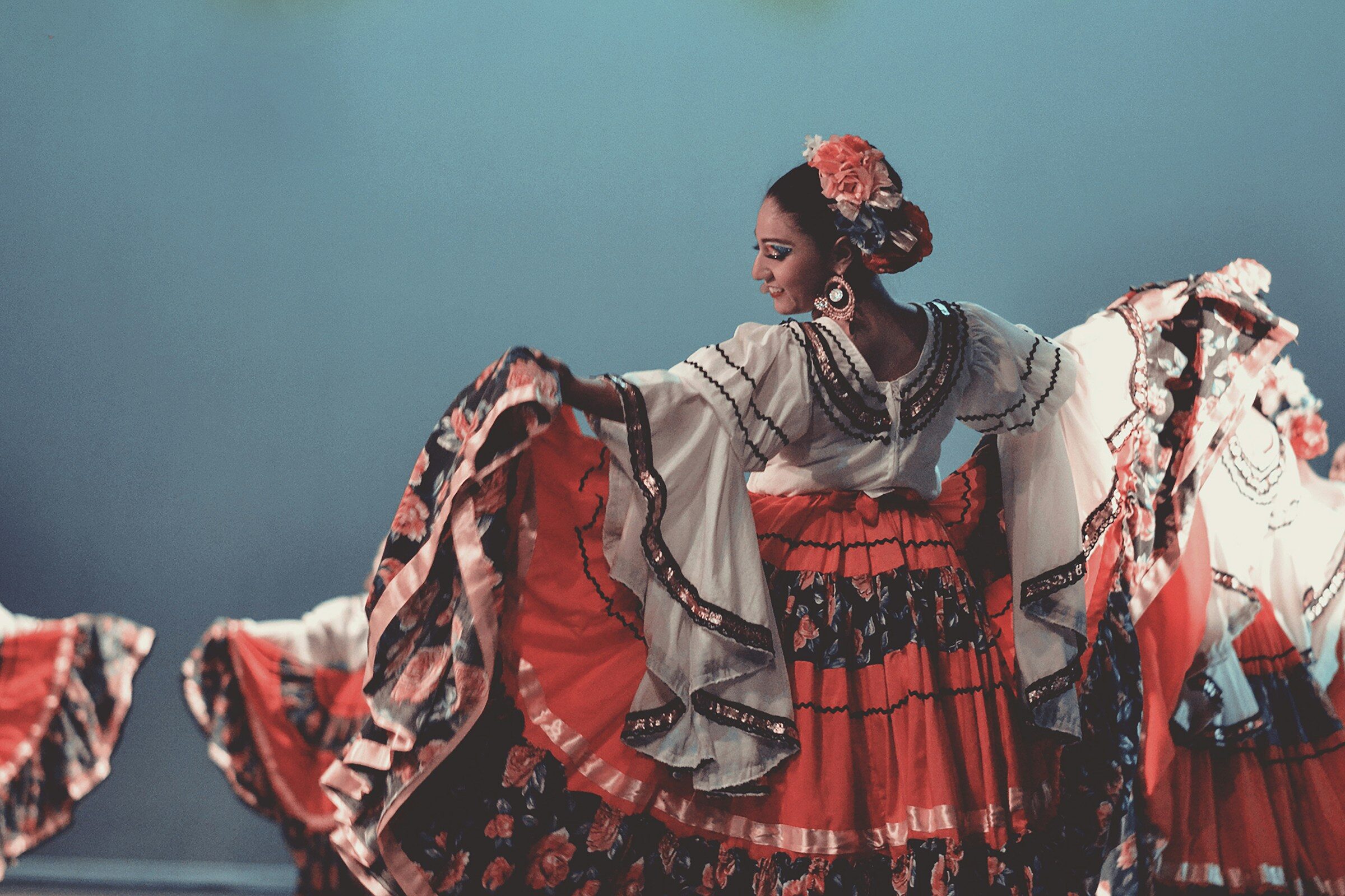 Black and white negative image of a Ballet Folklorico dancer. Dancer's back is turned toward the camera as she extends the sides of her skirt up and out 